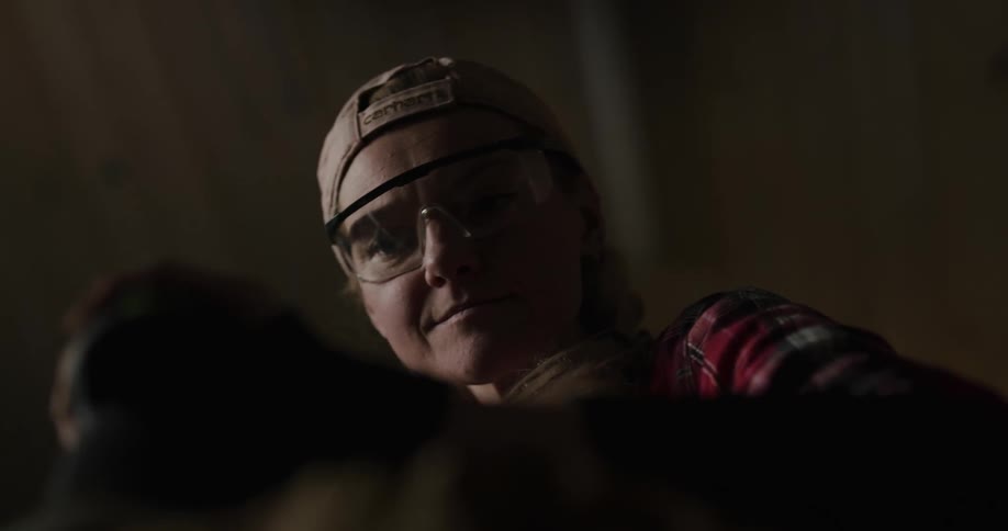 A woman in safety glasses smiling while using a sander on a piece of wood