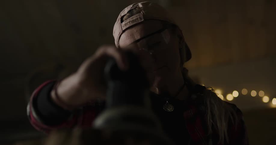 A woman with a hat and goggles sanding wood with an electric sander