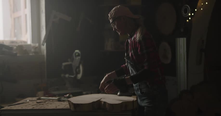 A person uses a power sander on a large piece of wood in a workshop