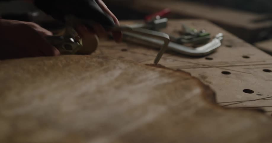 A person in a workshop using a tool on a piece of wood on a table