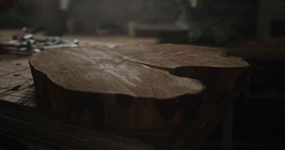 A woodworker using a chisel on a large piece of wood in a dim workshop