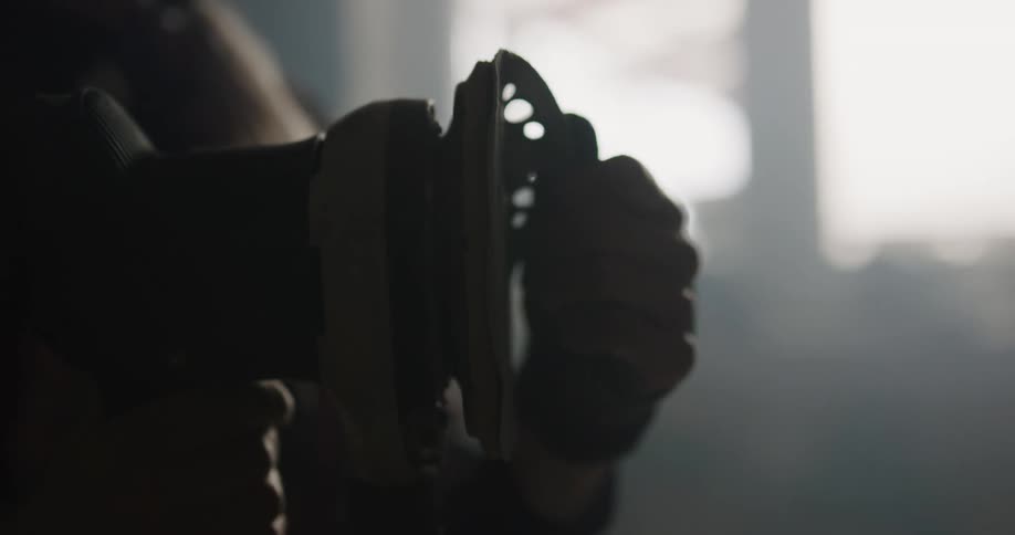 A person in a room holding a tool with a wall and window in the background