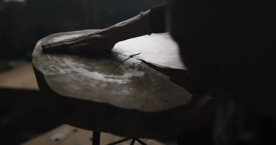 A woman rubs her hand over a tree stump that has been made in to a table as she polishes it