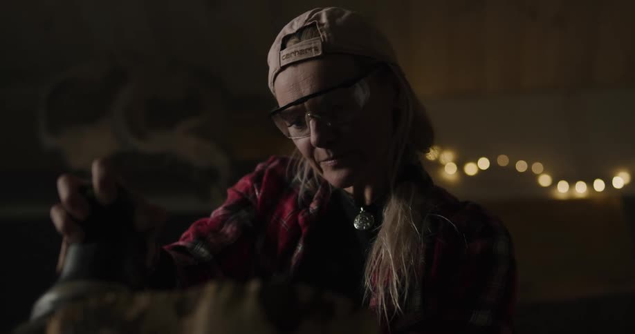 A woman with a hat and goggles sanding a piece of wood with an electric sander