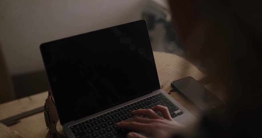Woman typing on a laptop with a replaceable screen inside a dimly lit room