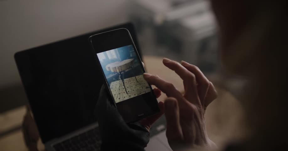 A woman is checks photos on her phone before using a laptop