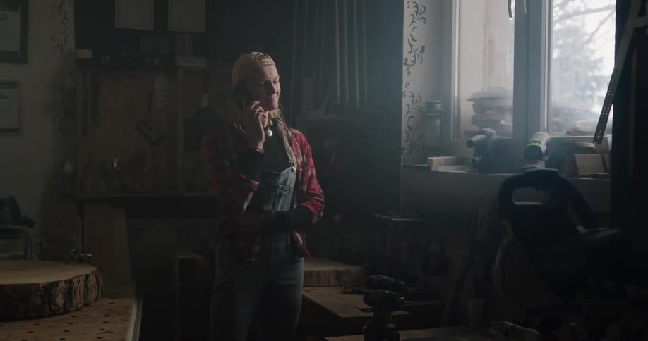 A woman smiling and nodding after answering a phone in a woodworking shop