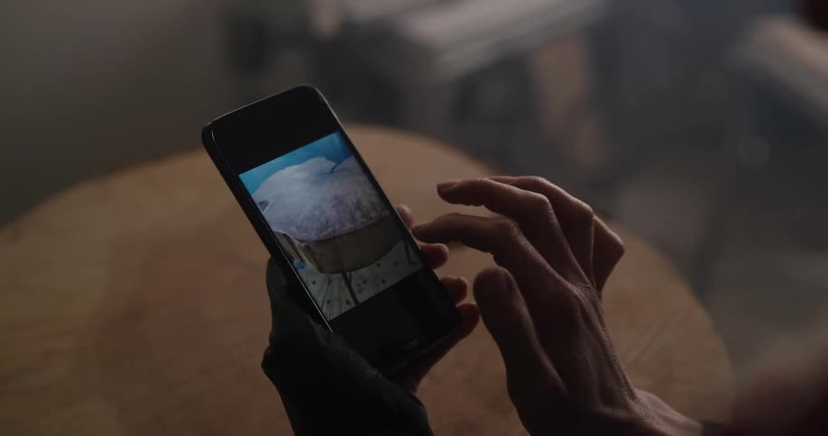 A woman taps on her phone and scrolls through photos of a tree stump table