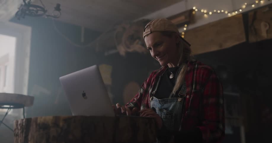 A woman smiling while using a smartphone and laptop in a dimly lit room