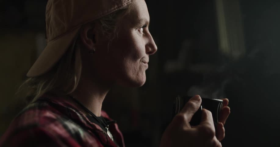 Woman stands in dark area drinking from steaming cup