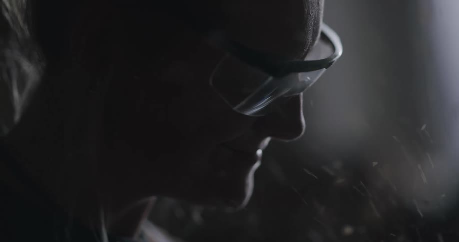 Sawdust flying around a womans face with safety glasses in a dark workshop