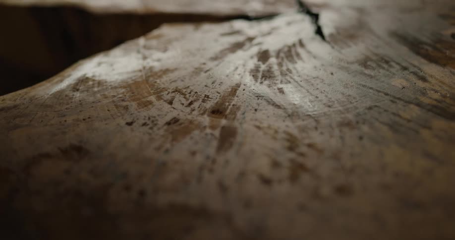 A person runs a paintbrush over a wood slab that has been sanded down