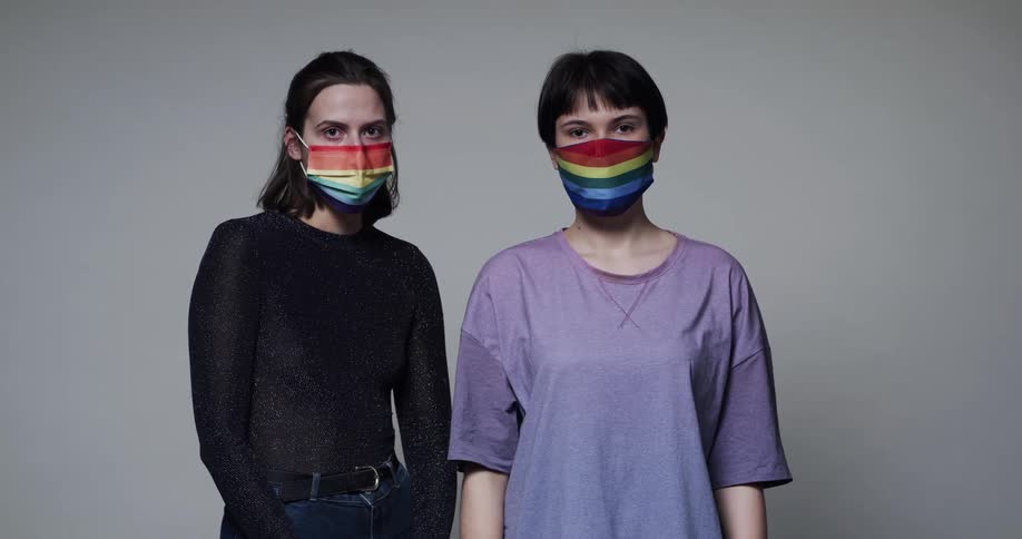Young lesbian couple puts on face masks with the gay pride flag on them