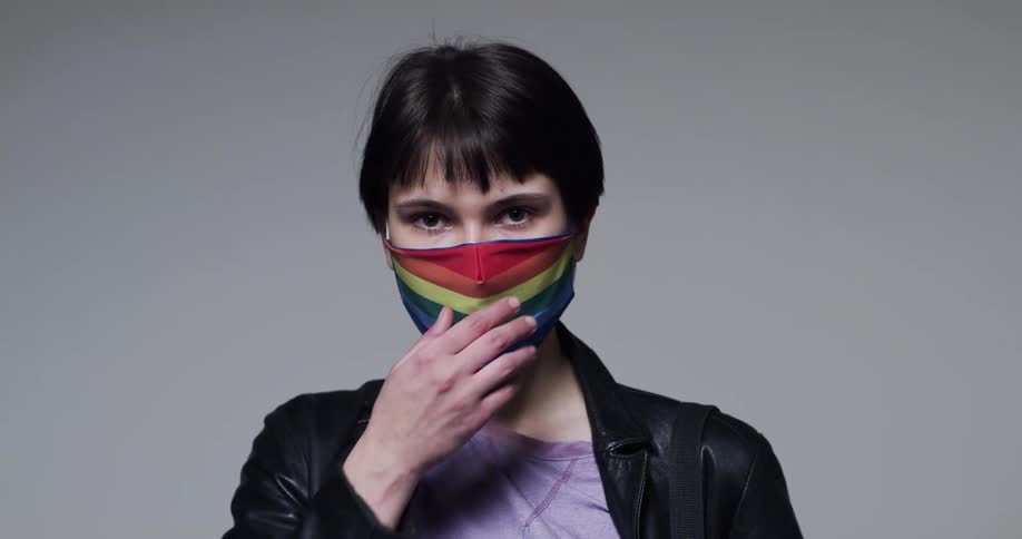 A woman pulling down a rainbow face mask to reveal a smile