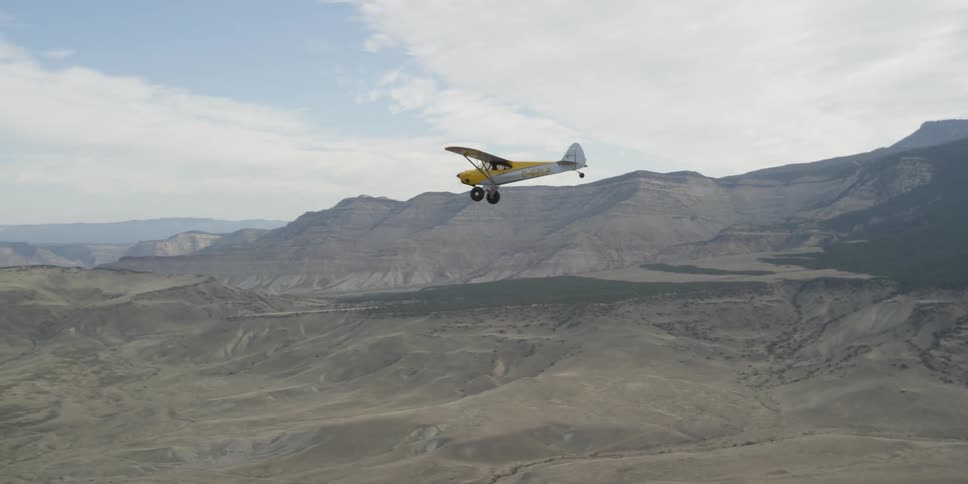 A yellow plane flies over a desert