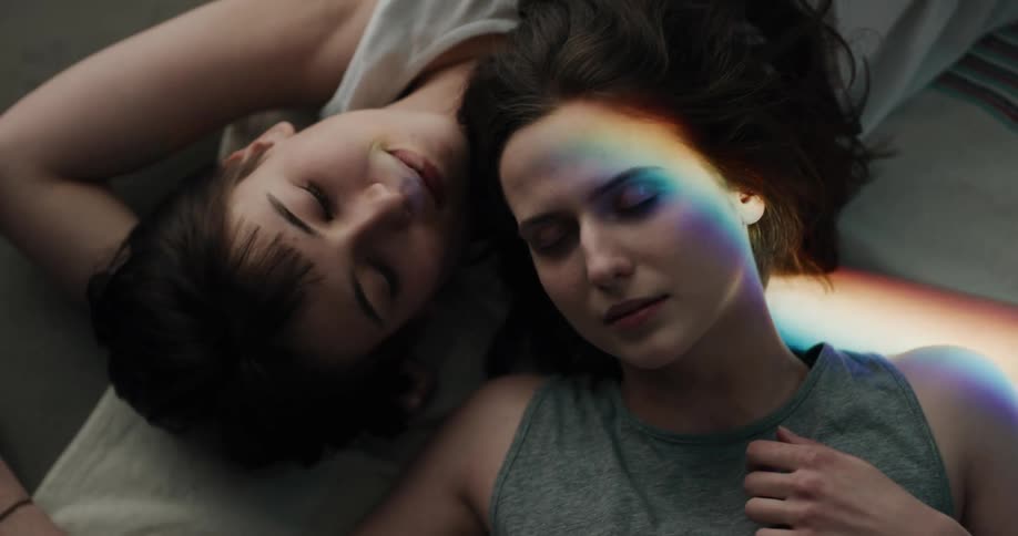 Two women lie sleeping together as prism light moves across them