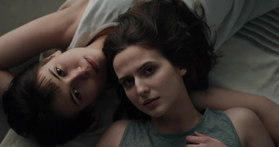 A rainbow light shining on a cuddling lesbian couple while lying down