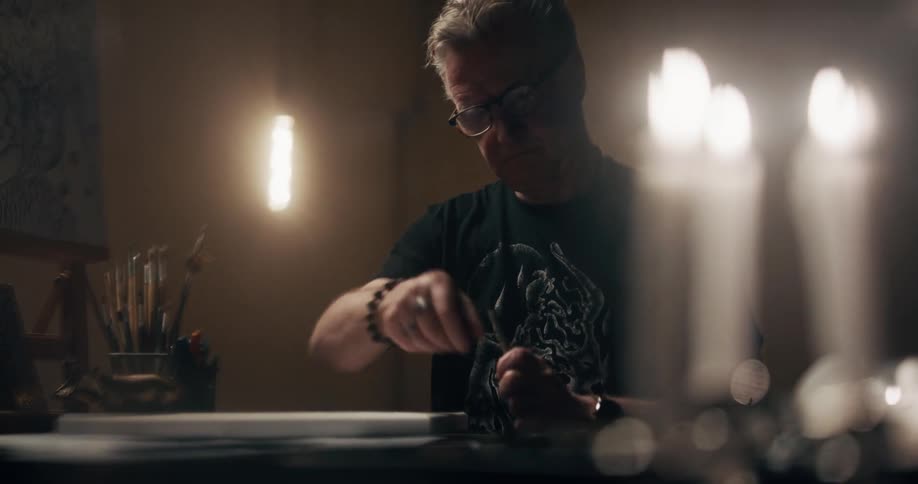 A man with glasses in a room with candles and flames in the foreground