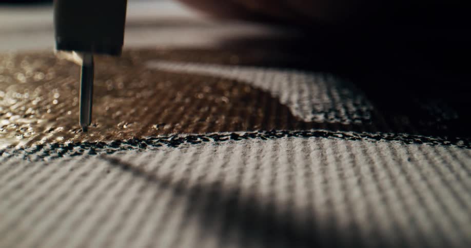 A pen making small black marks on a white canvas art work