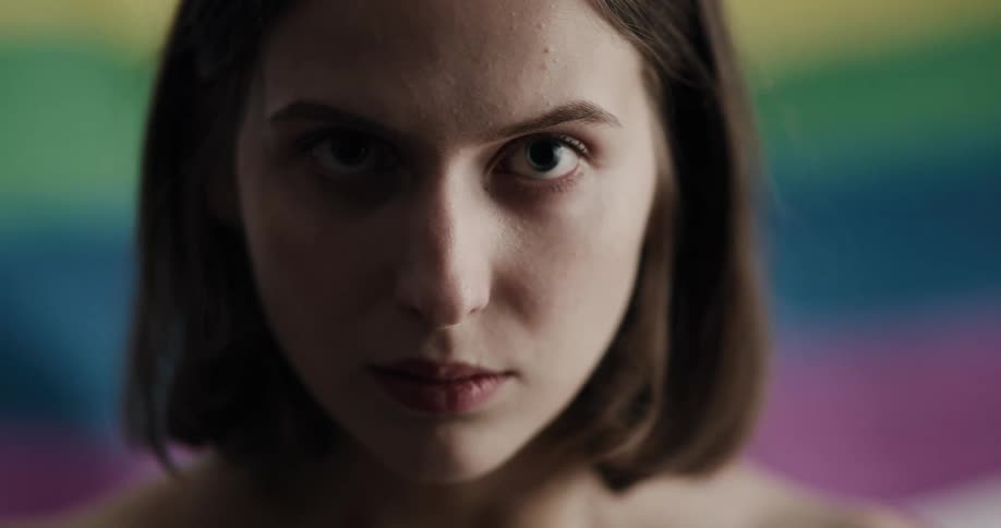 Woman standing in front of a waving gay pride flag looks up at the camera