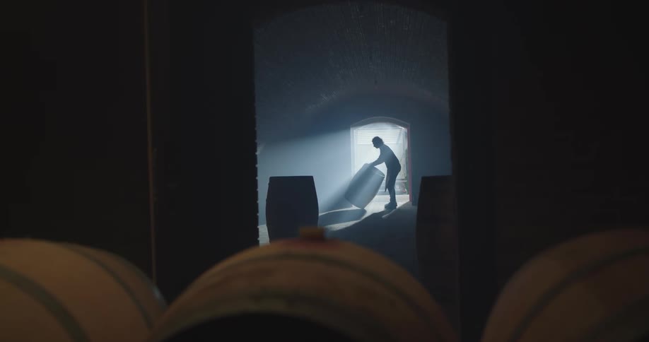 A man opens the wide door to a room full of wooden barrels and drags more barrels inside