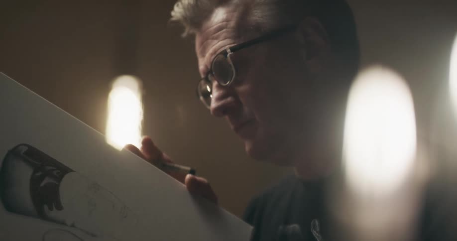 A man holds up and closely examines a canvas with a partial drawing