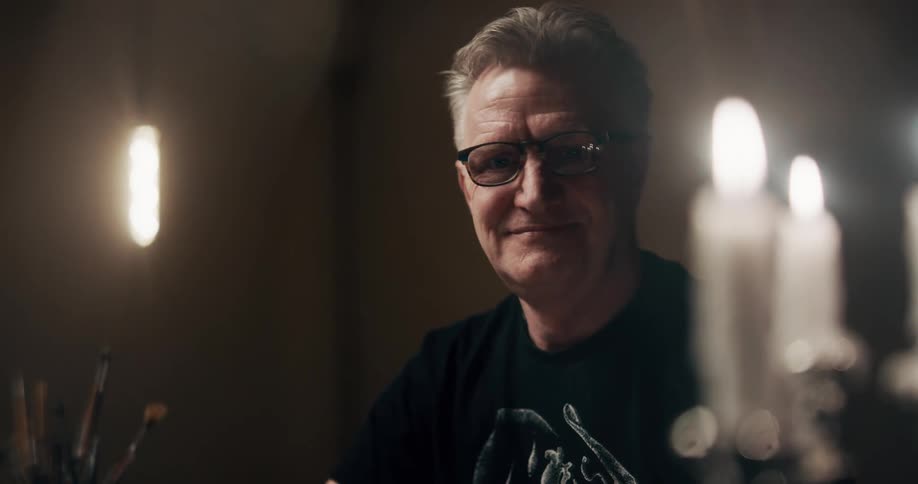 Man sitting in room lit by melting candles looks up and smiles
