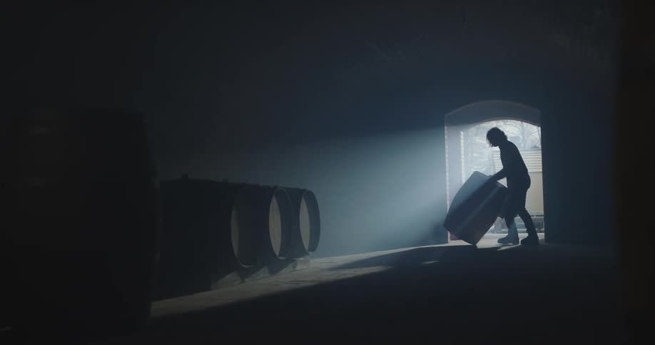 A man opens double doors and lets sunlight into a dark room filled with wooden barrels