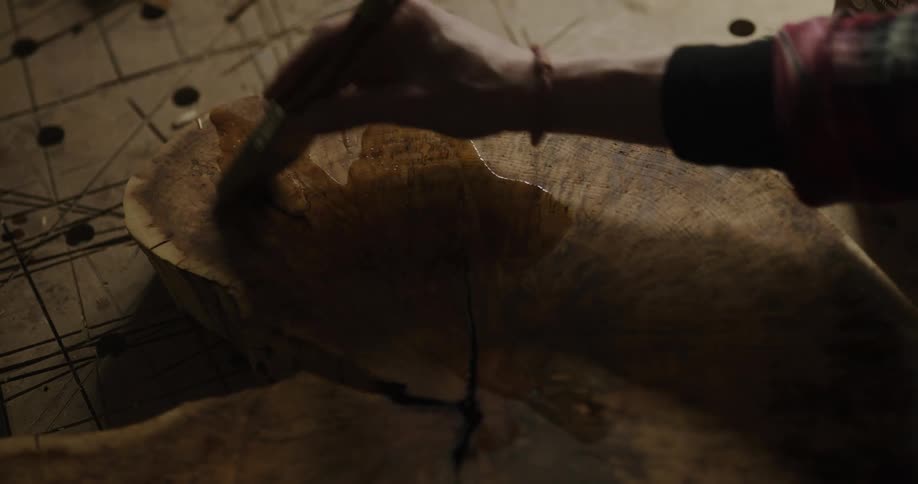 A woman pours oil on a slab of wood and brushes it on in slow movements