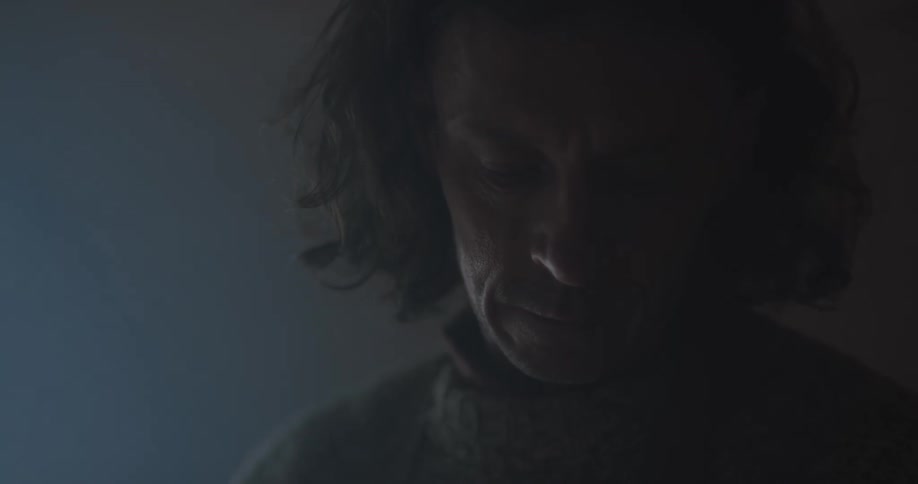 A man looks down as he stands in a dark room