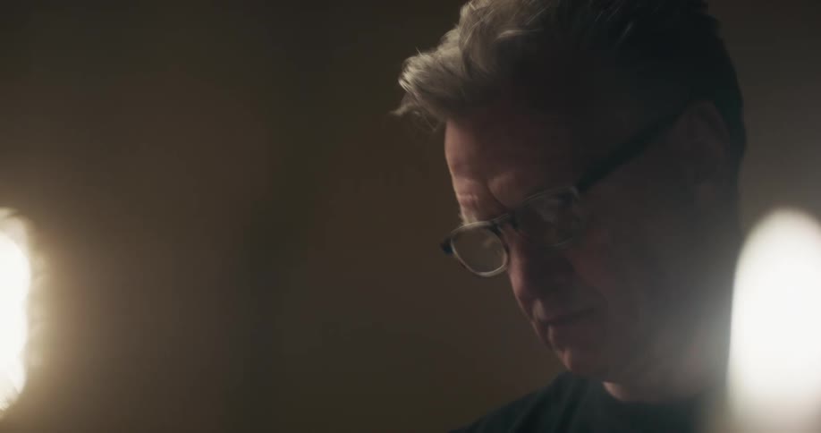 A man with glasses in a room with a candle and flame in the foreground