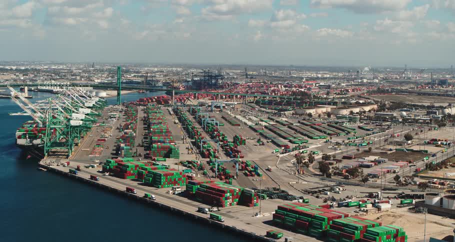 Aerial view of a shipping dock next to a body of water at the edge of a city with trucks driving by down below