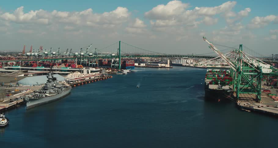 A shipping dock at the edge of a city next to a river and a suspension bridge during the day