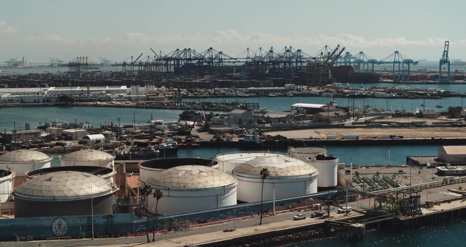 Multiple buildings and cranes line an industrial shipping port where there are multiple large storage structures