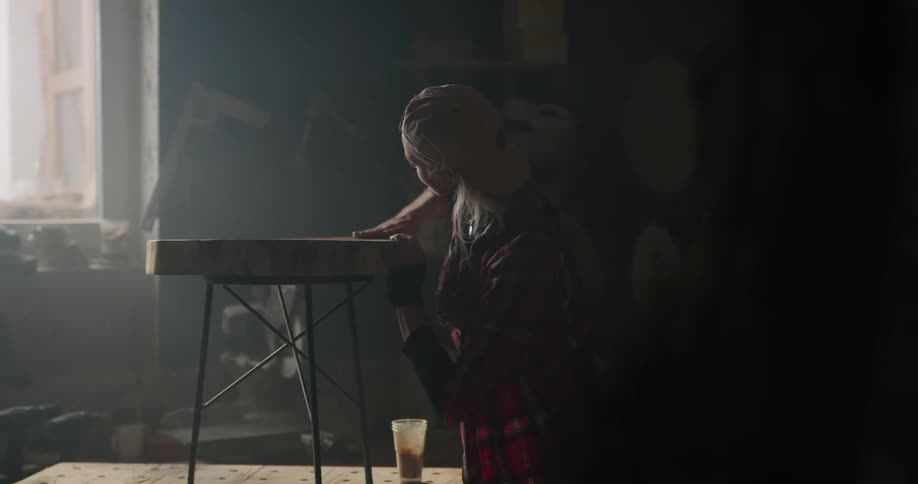 A woman with a hat in a workshop rubbing oil on a table