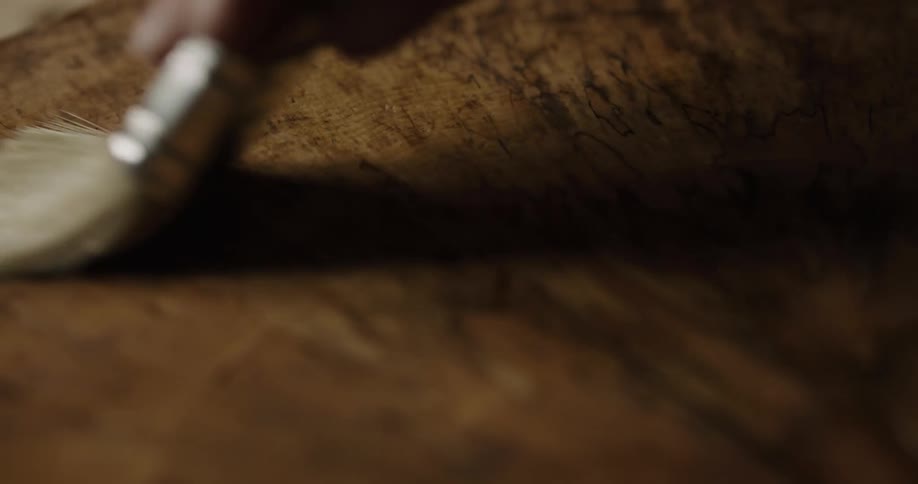 A person is using a paint brush to paint wood