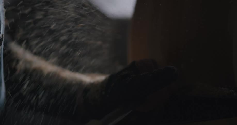 A person with gloves and goggles shaving wood on a spinning wheel