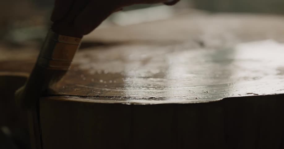 A person brushes oil on a wood slab with slow back and forth motions