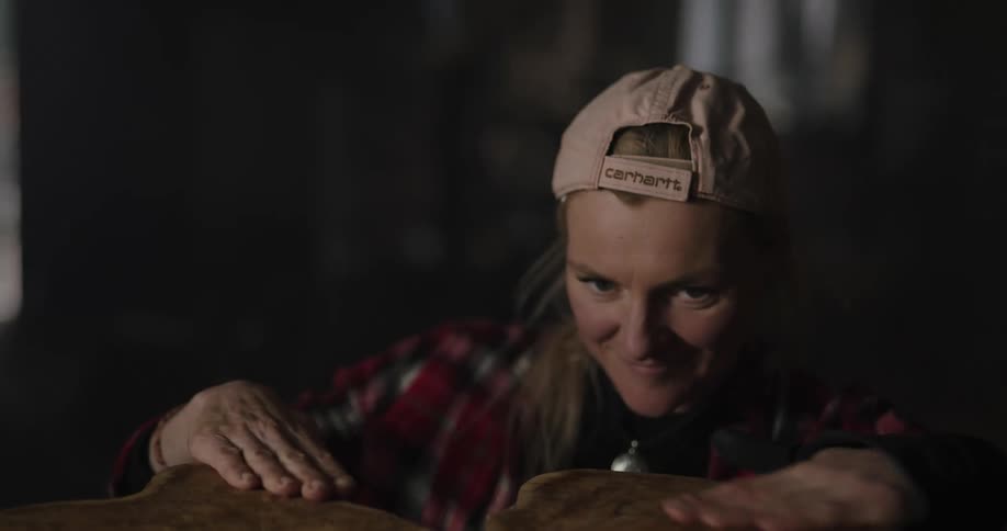 A woman flips over a cut tree trunk and rubs it and smiles