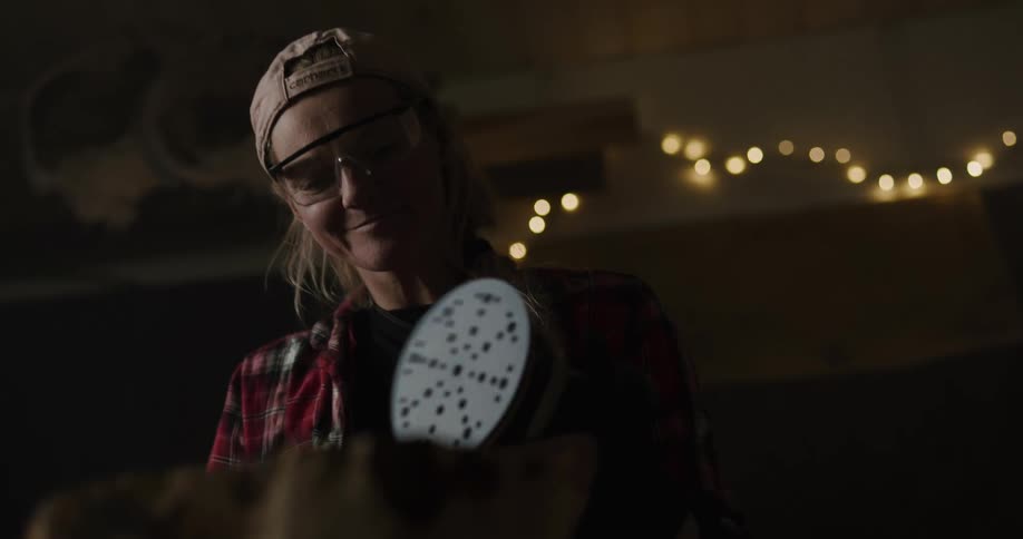 A woman puts on her glasses and starts to sand furniture