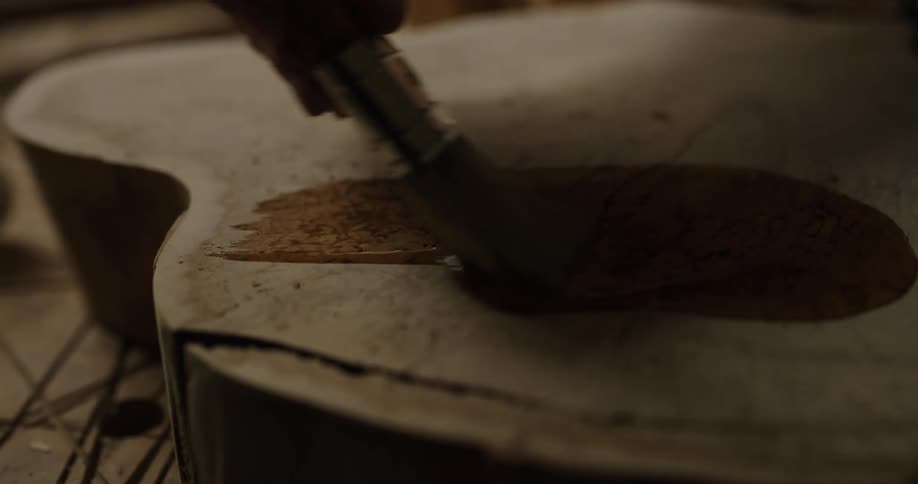 Person pours stain onto horizontal panel cut from tree trunk before spreading it with a brush