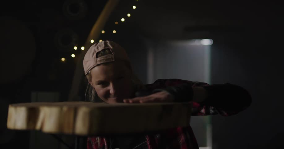 Blonde woman flips wooden table made from horizontal slice of tree trunk right side up in shadowy room and dusts it off with her hand