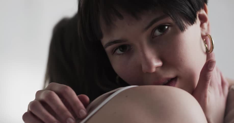 A woman looks over the shoulder of the woman she is embracing to gaze into the camera as she strokes her partners back