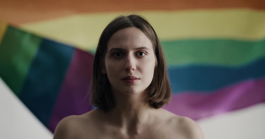 Half naked woman looks at the camera in front of a waving lgbt flag