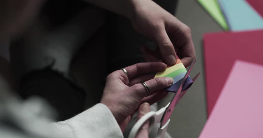A woman helps a younger man cut a heart out of rainbow printed paper