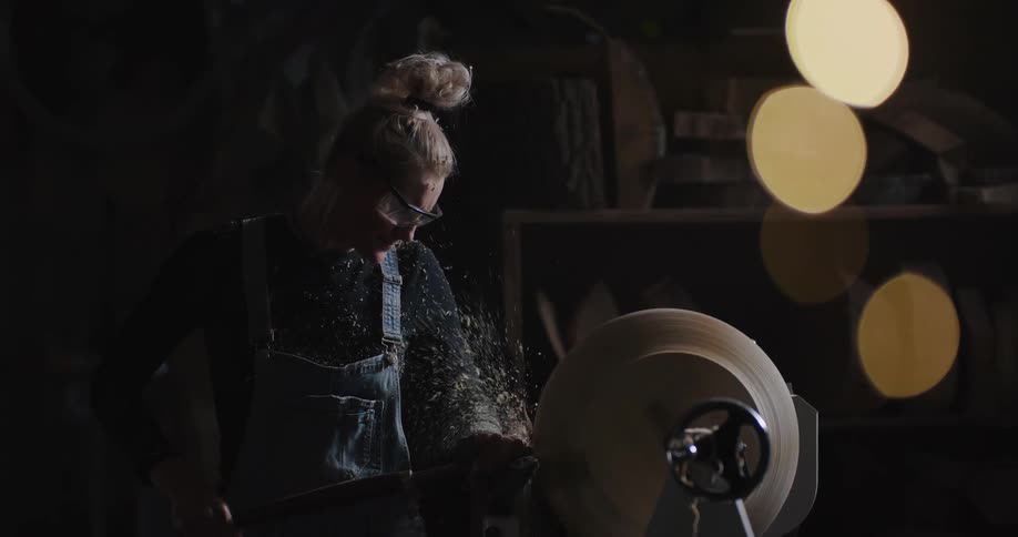 A person in a room with goggles shaving wood on a spinning wheel