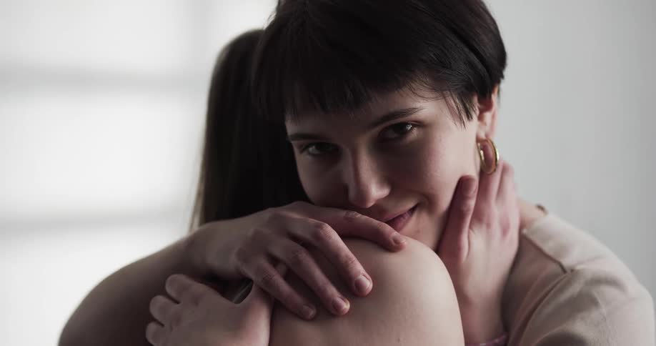 Two women embrace while one stares at the camera