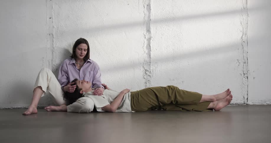 A woman caresses her girlfriends hair as she sits on the floor with her girlfriends head in her lap
