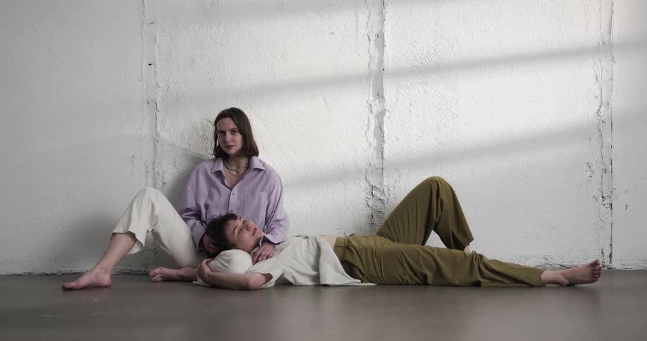 Young lesbian copule resting on the floor of a room looking at the camera