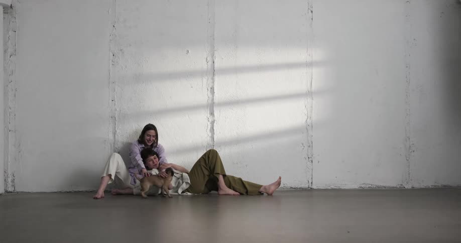 A puppy runs across a room to play with a pair of young women resting on the floor